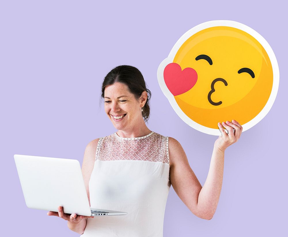 Woman holding a kissing emoticon and using a laptop