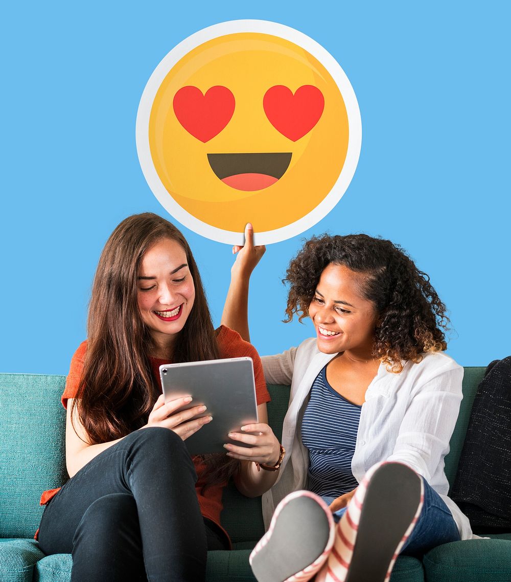 Women holding a heart eyes emoticon and using a tablet