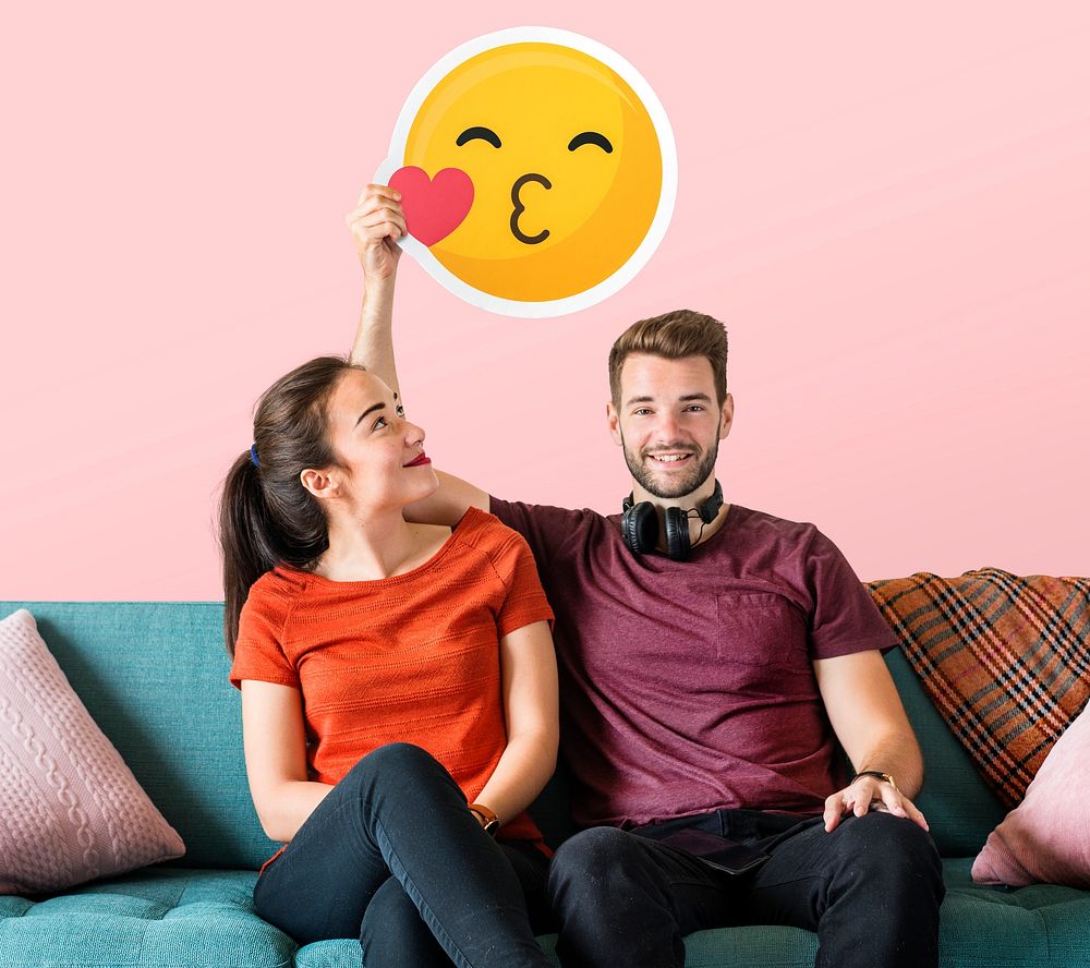 Cheerful couple holding a kissing emoticon