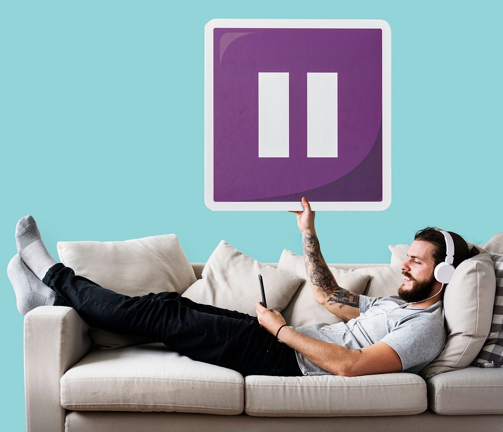 Male on a couch holding a pause button icon