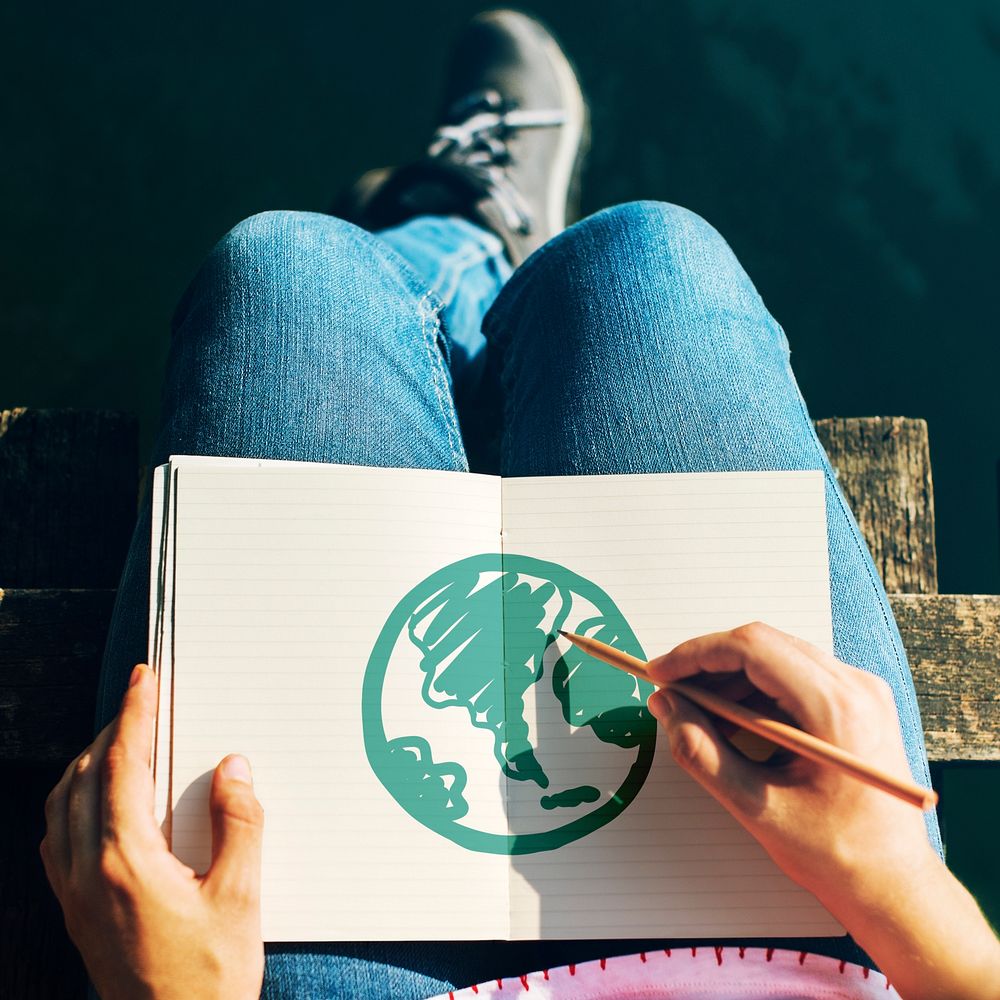 Woman drawing a green globe on a notebook