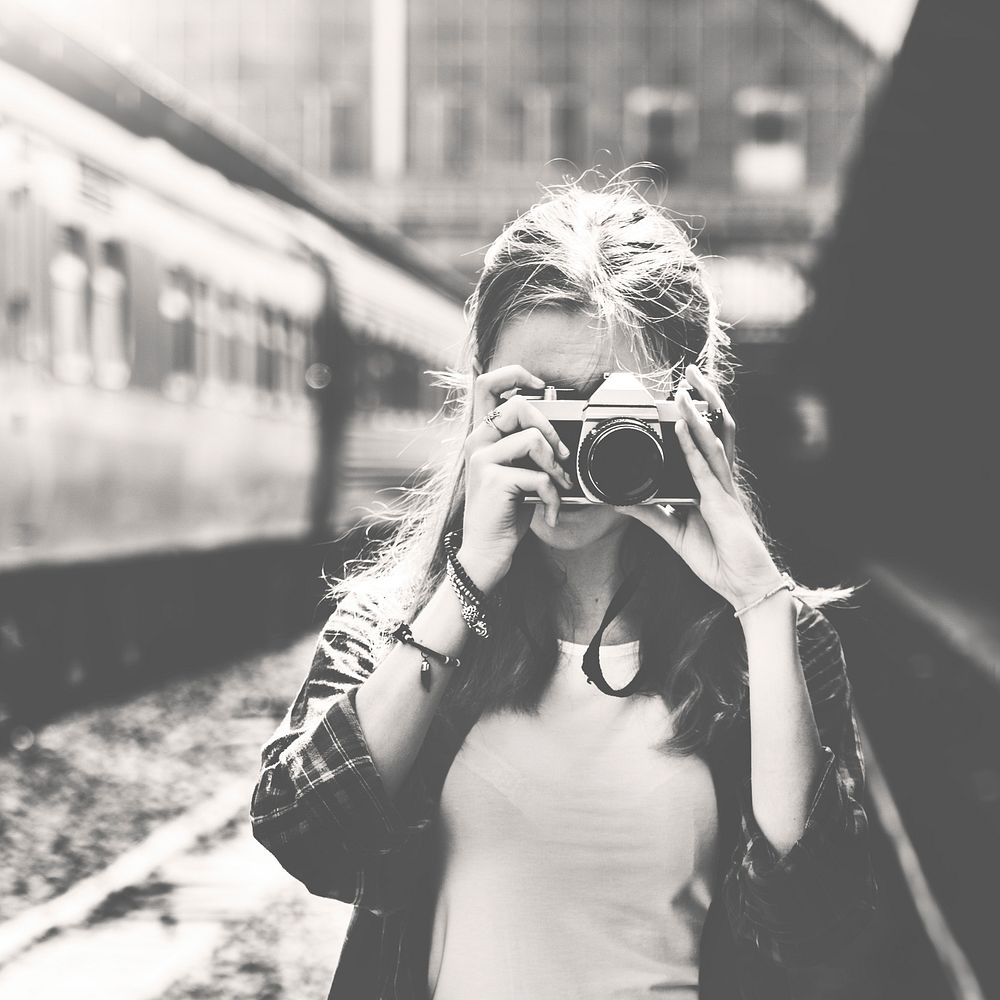 Woman using camera taking photo at train station grayscale