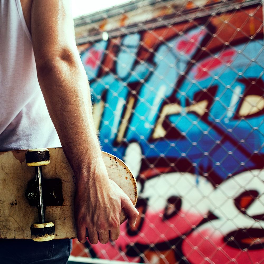 Closeup rear view of arm holding skateboard with graffiti wall background