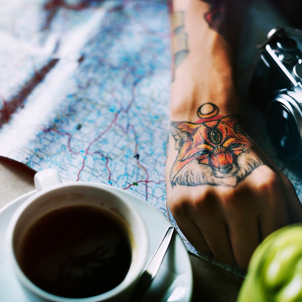 Closeup of tattoo hand with map and coffee cup