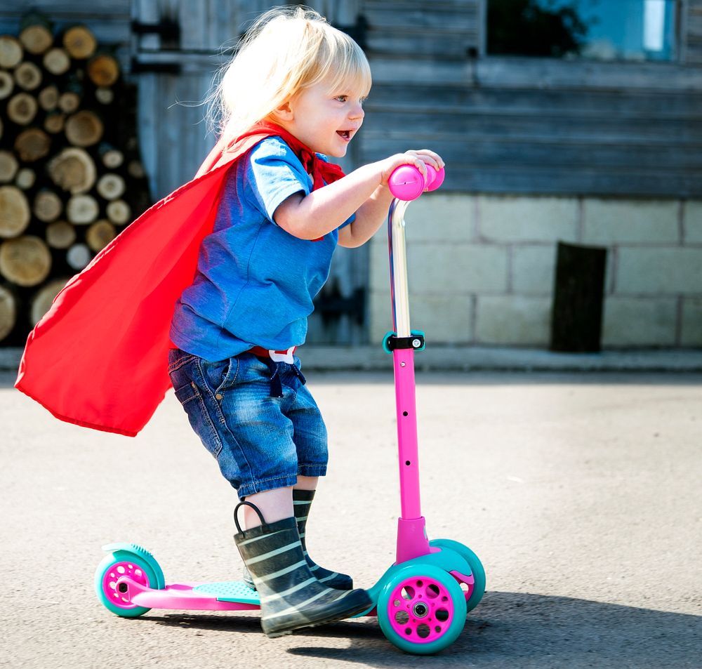 Little boy in superhero costume playing a scooter
