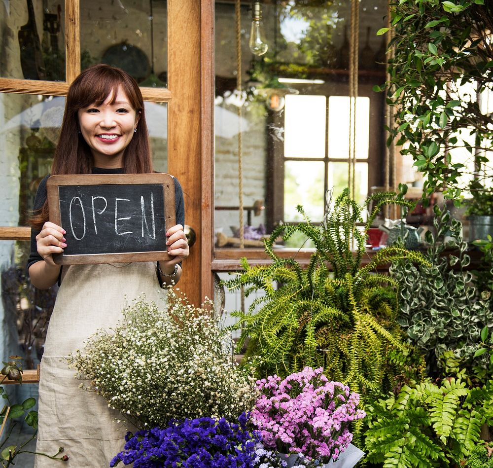Welcoming florist holding an open sign in front of a flower shop