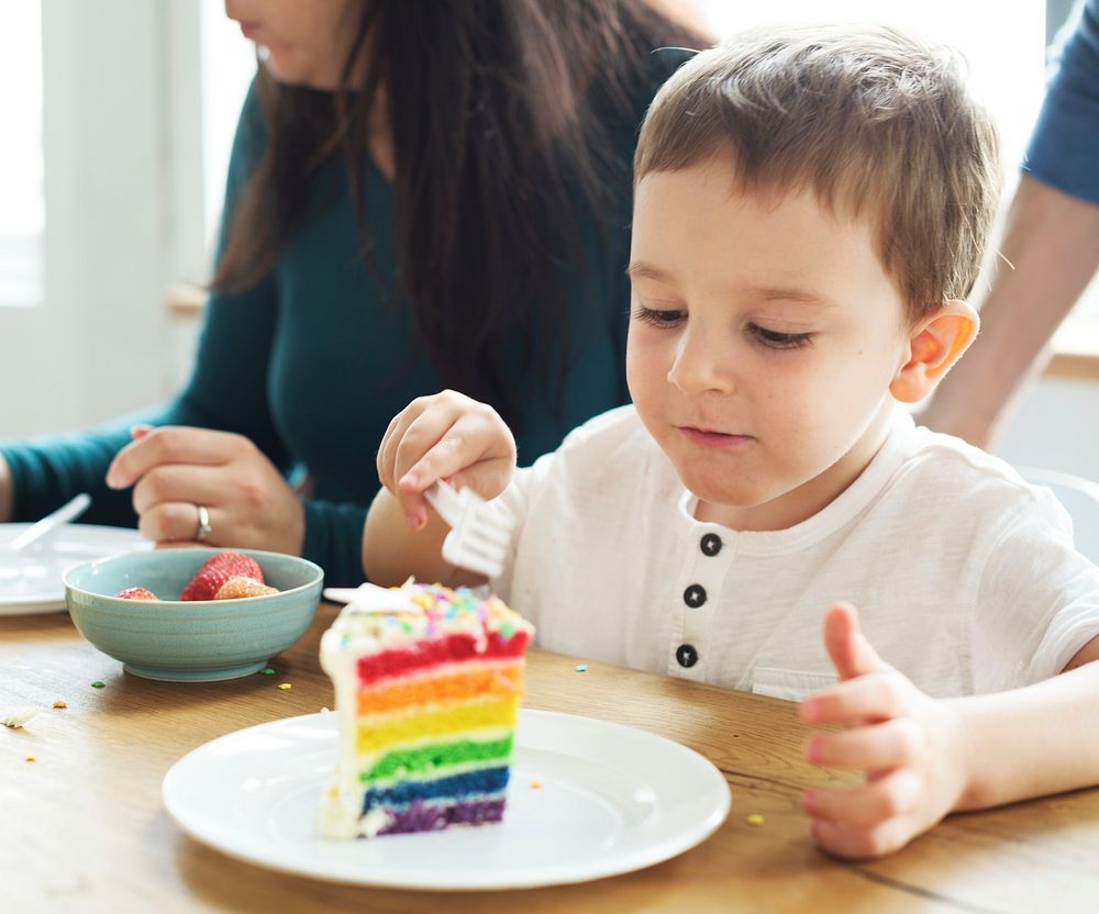 Little boy eating a rainbow colored cake