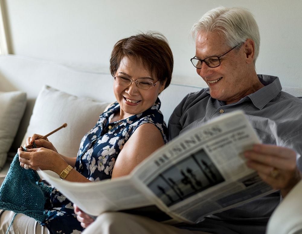 Senior couple in a living room reading a newspaper and knitting