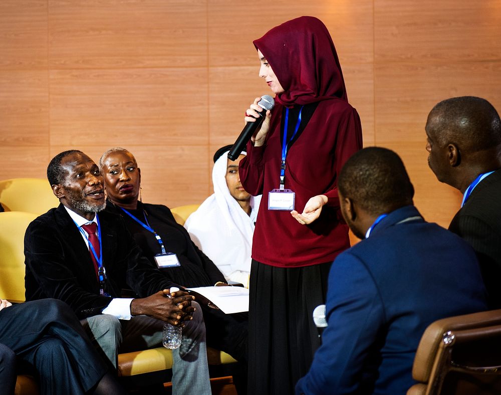 A Muslim Woman Speaking into a Microphone in a Group of Business Delegates
