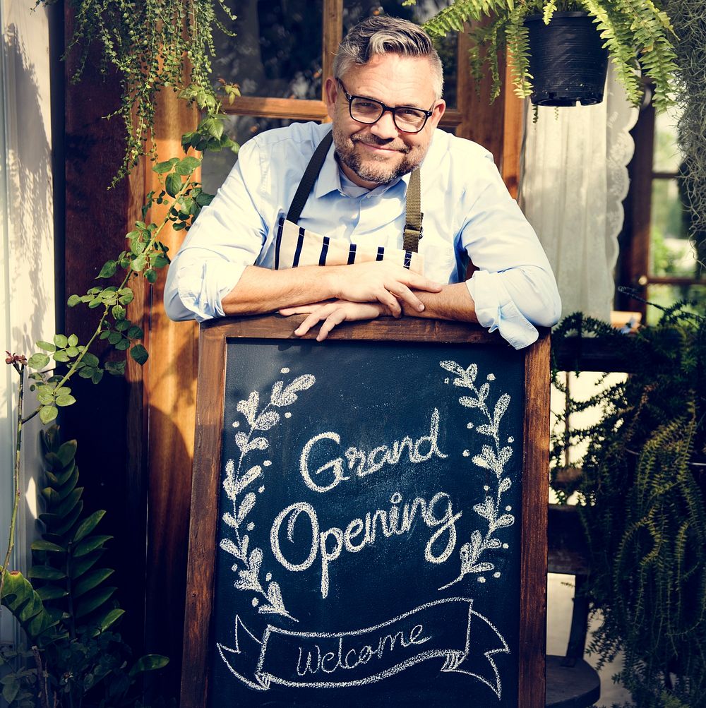 Man with grand opening blackboard in front the shop