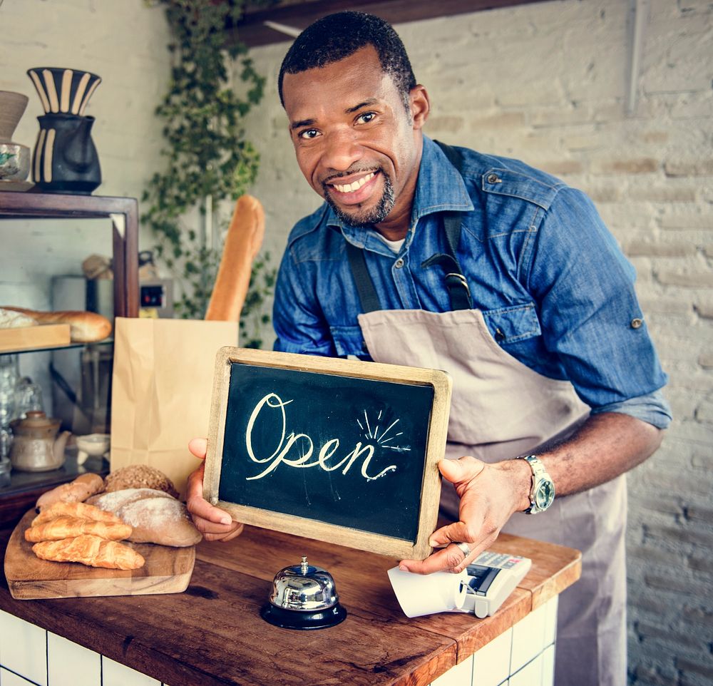 African Man Holding Open Sign in Bakery Shop