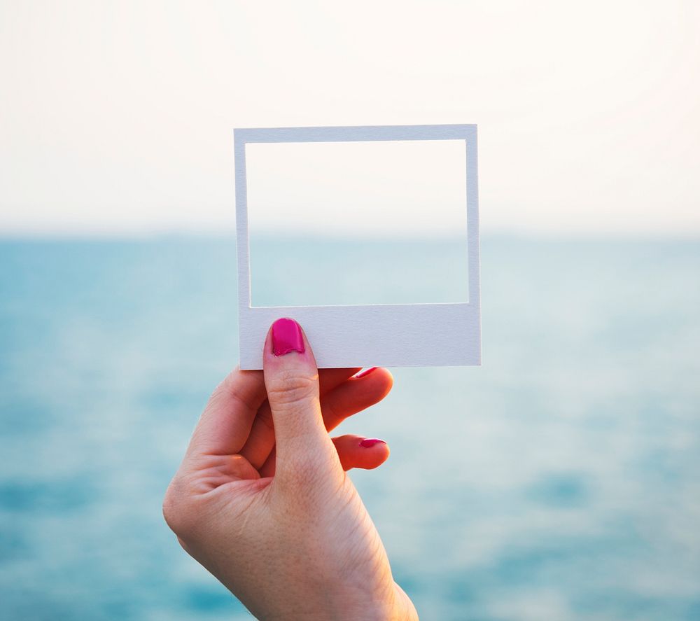 Hand holding perforated paper frame with ocean background