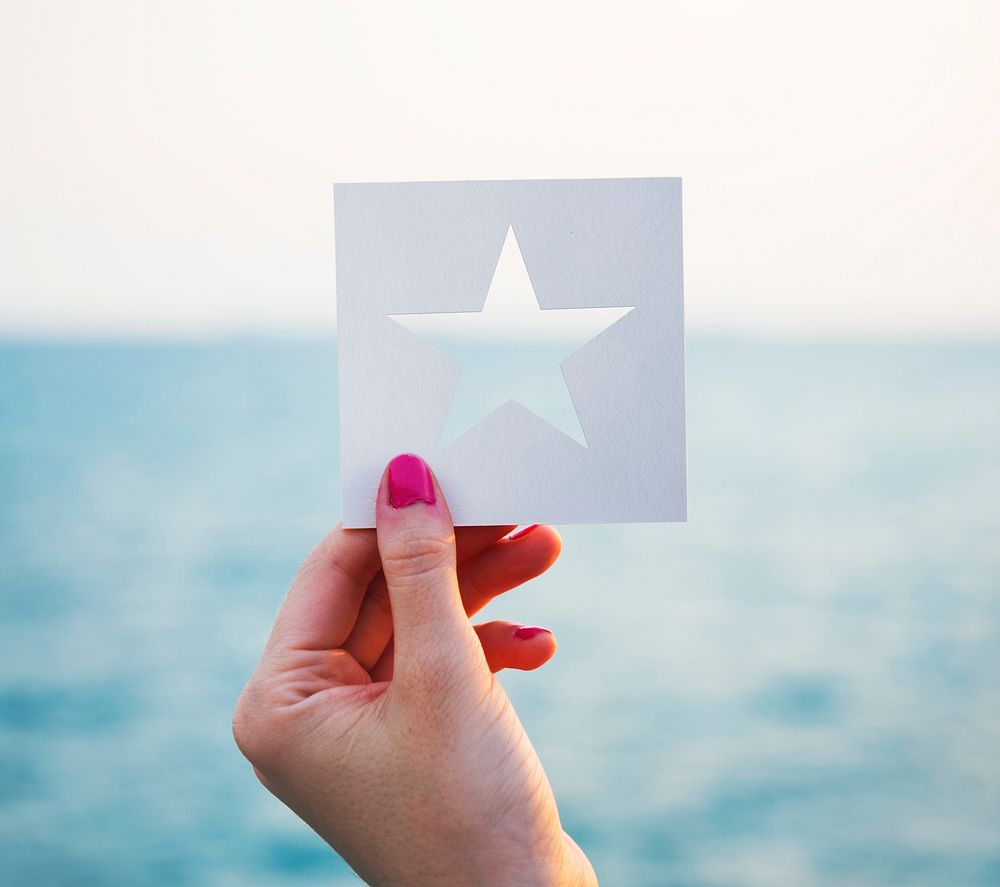 Hand holding perforated paper star shape with ocean background
