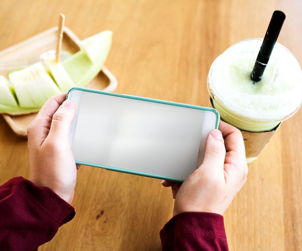 Hands using mobile phone with fruit and drink on the table