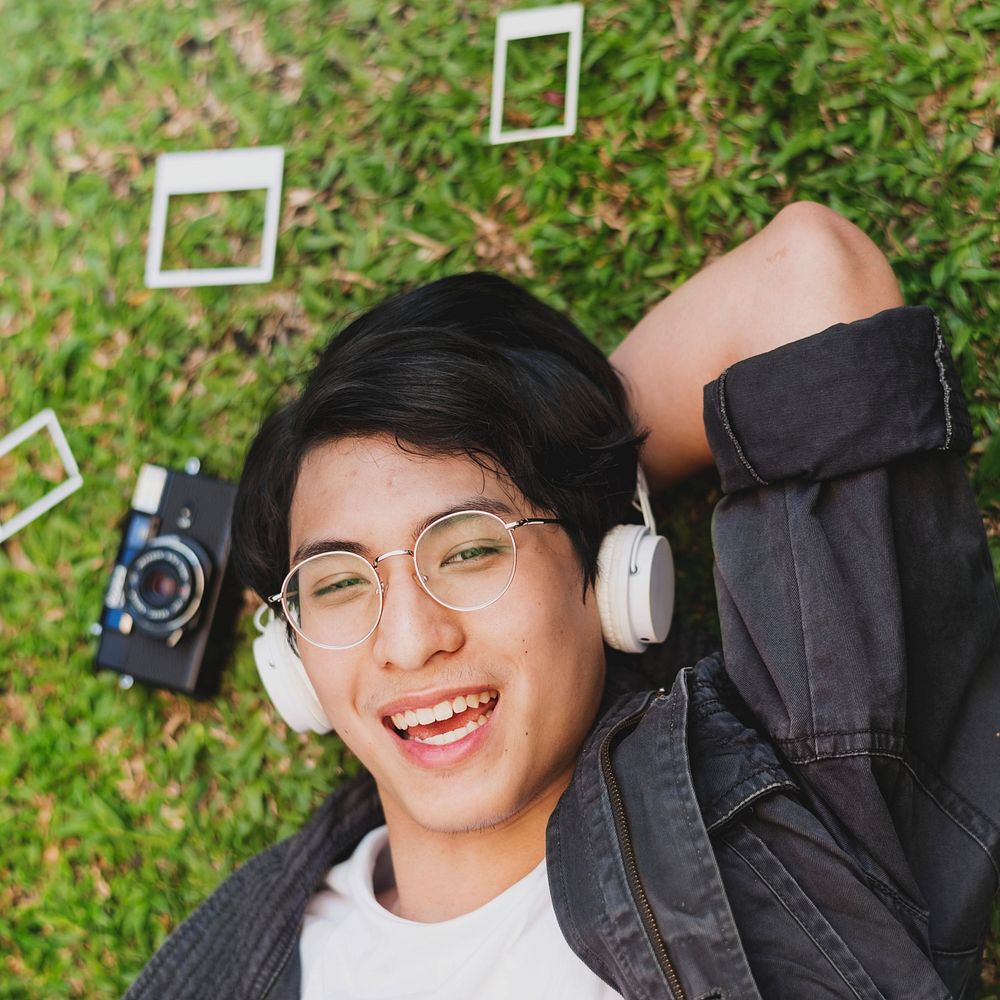 Young asian man lying on the grass listening to music