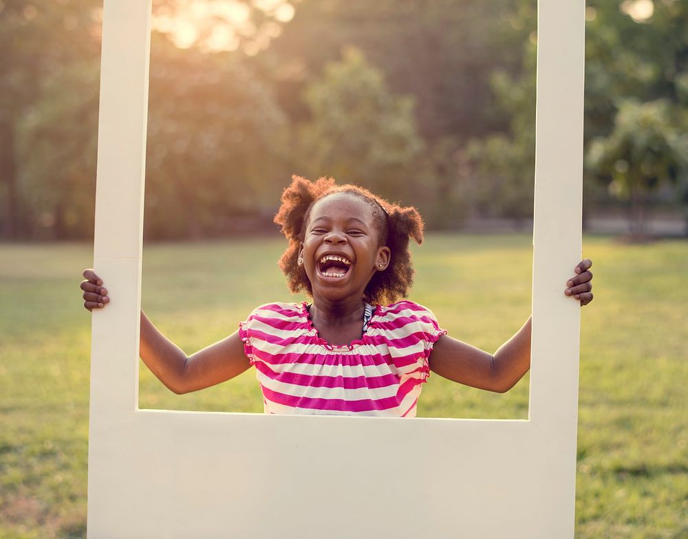 African descent girl is holding frame in a park