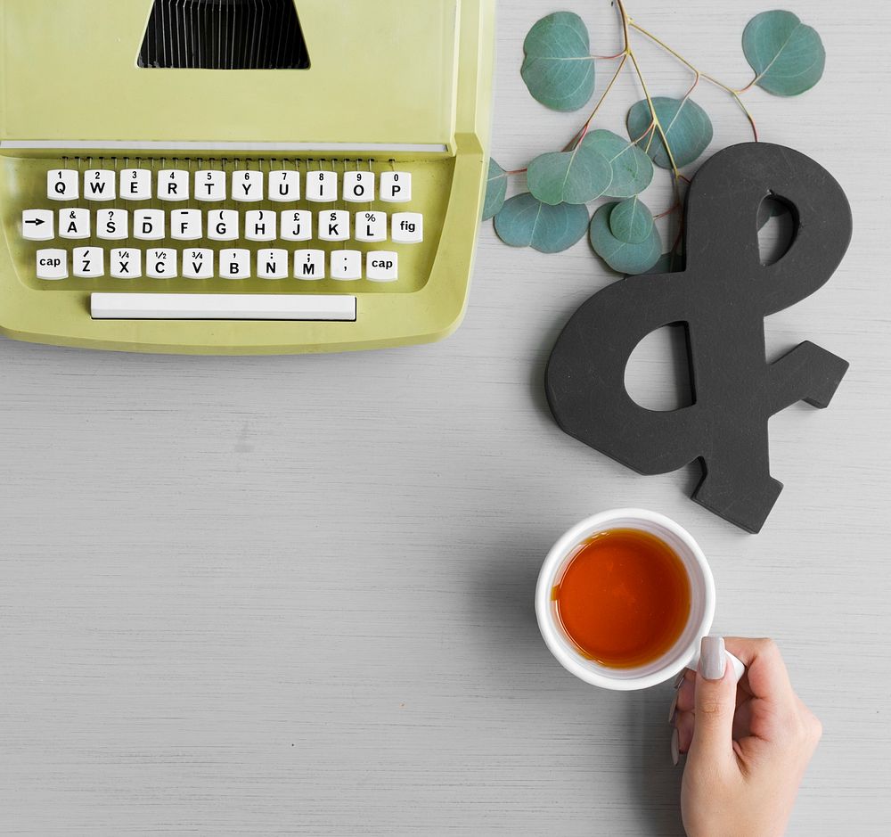 A hand holding a cup of tea featuring a retro typewriter