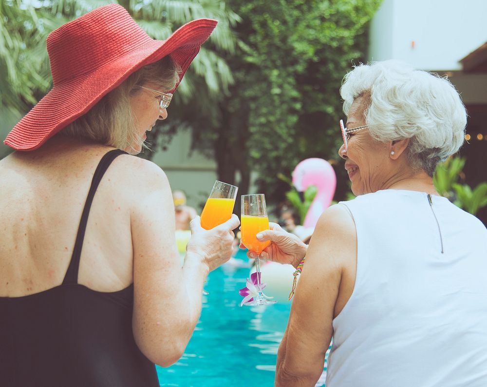 Senior couple women with orange juice by the pool together