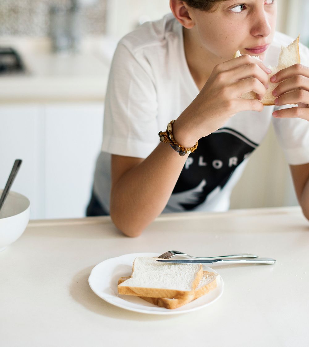 Young caucasian man eating sandwich in kitchen