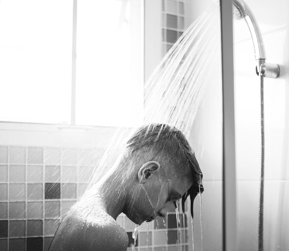 Young caucasian man showering in bathroom grayscale