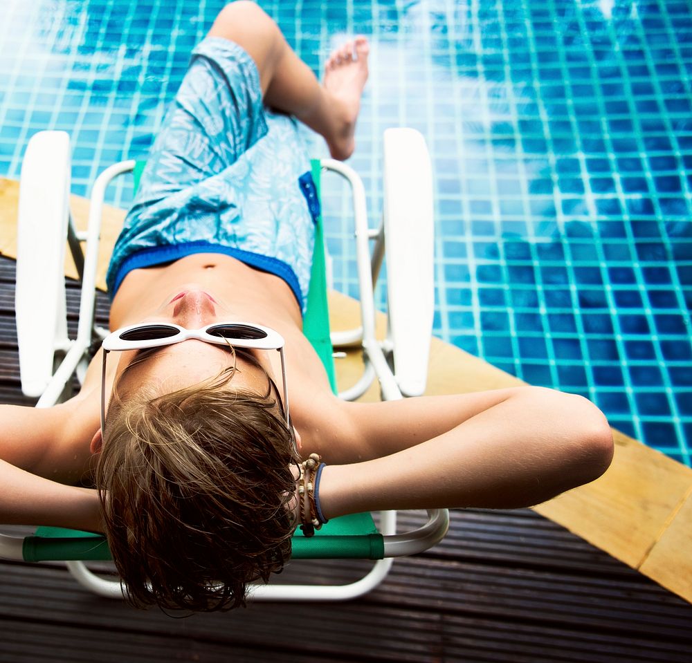 Young caucasian boy enjoying sunbathing by the pool