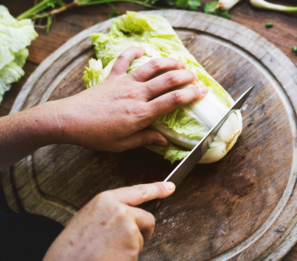 Hands chopping chinese cabbage on a wooden cutting board