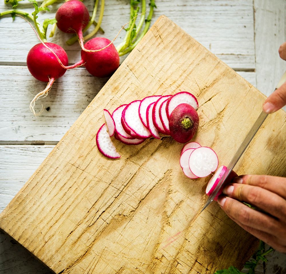 Hands chopping radish on wooden cutting board
