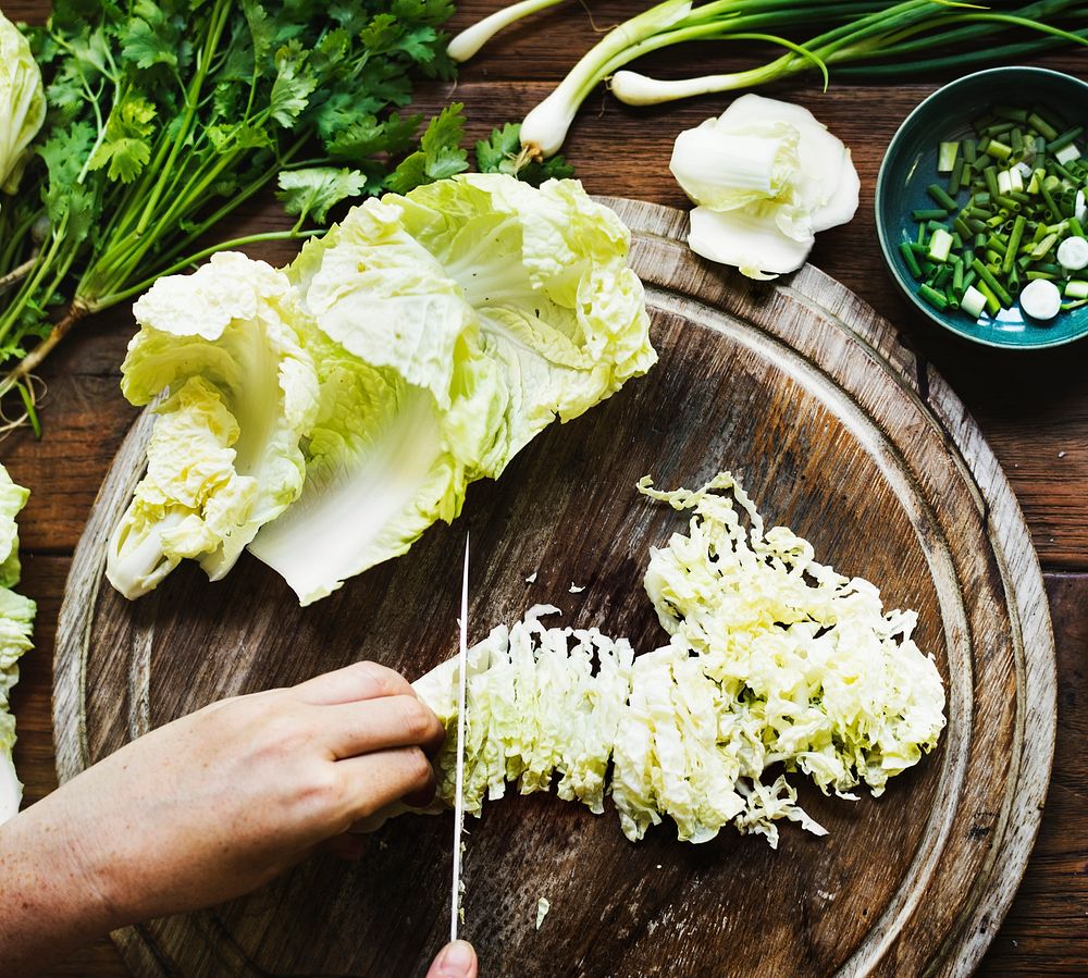 Aerial view of hands with knife cutting chinese cabbage on wooden cut board