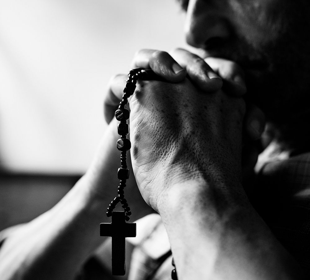 Cloesup of hands holding cross praying grayscale