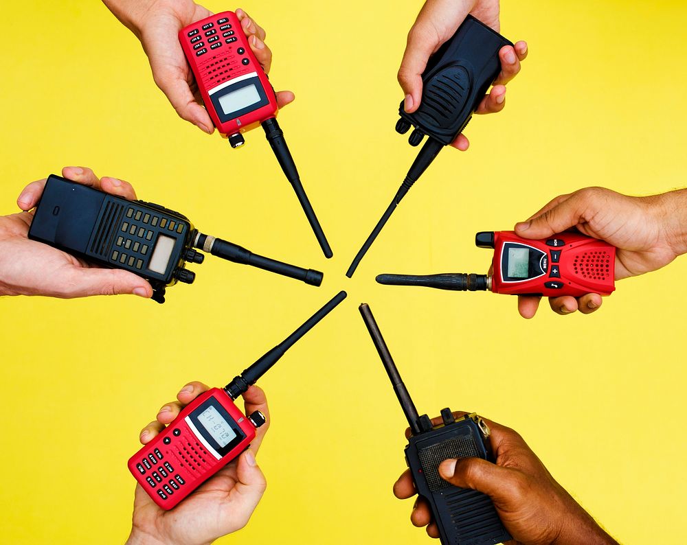 Group of hands holding portable two way radios with yellow background