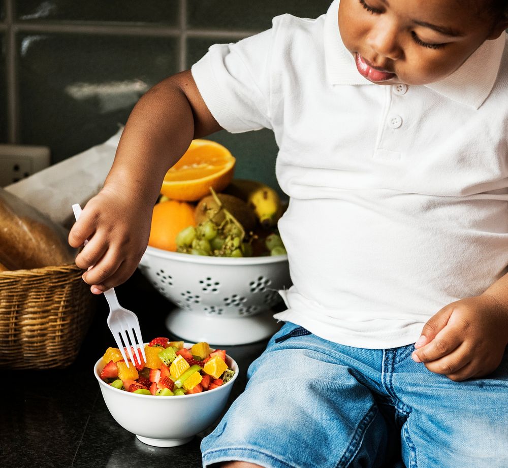 Black kid with fruit salad in the kitchen