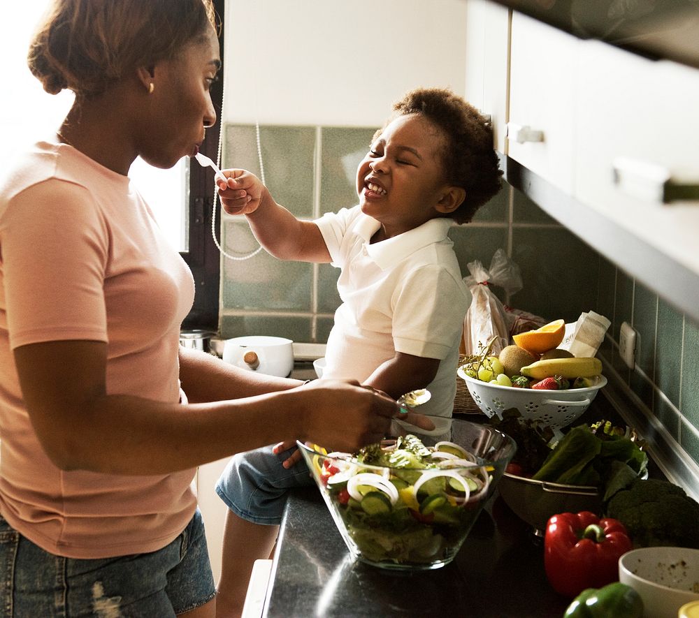 Black kid feeding mother with cooking food in the kitchen