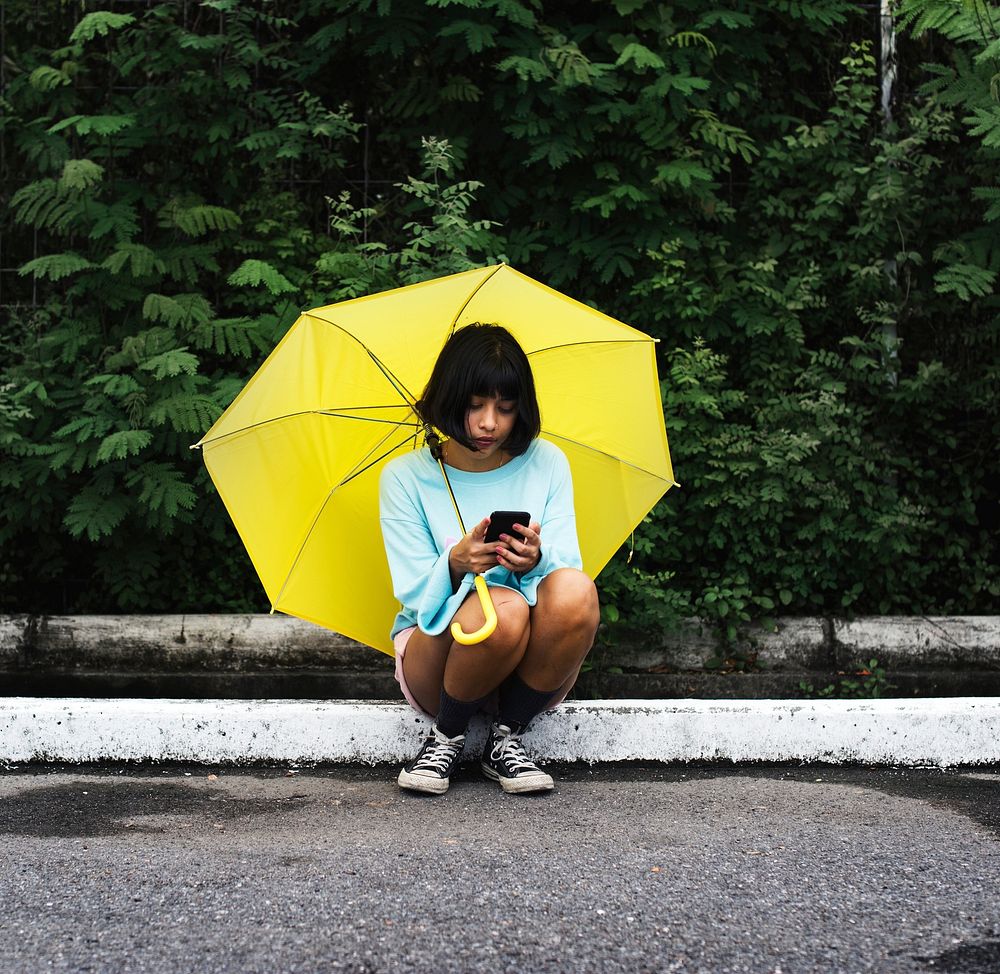 An Asian woman sitting and using mobile phone under an umbrella