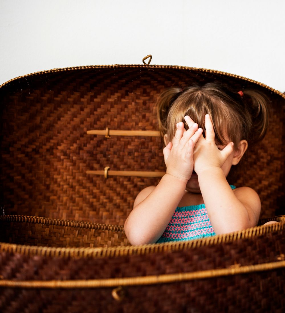 Little girl sitting in the basket and hands covering face
