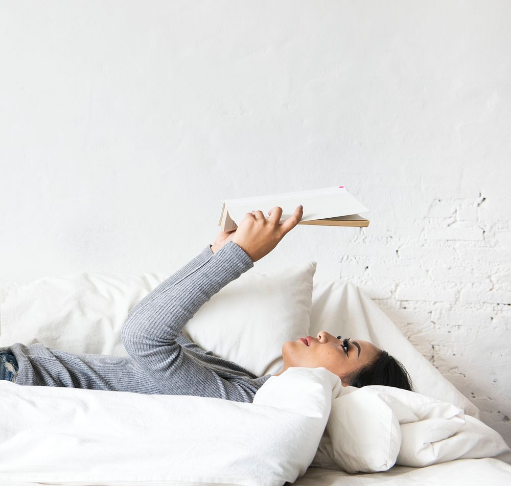 Asian woman lying on bed reading book