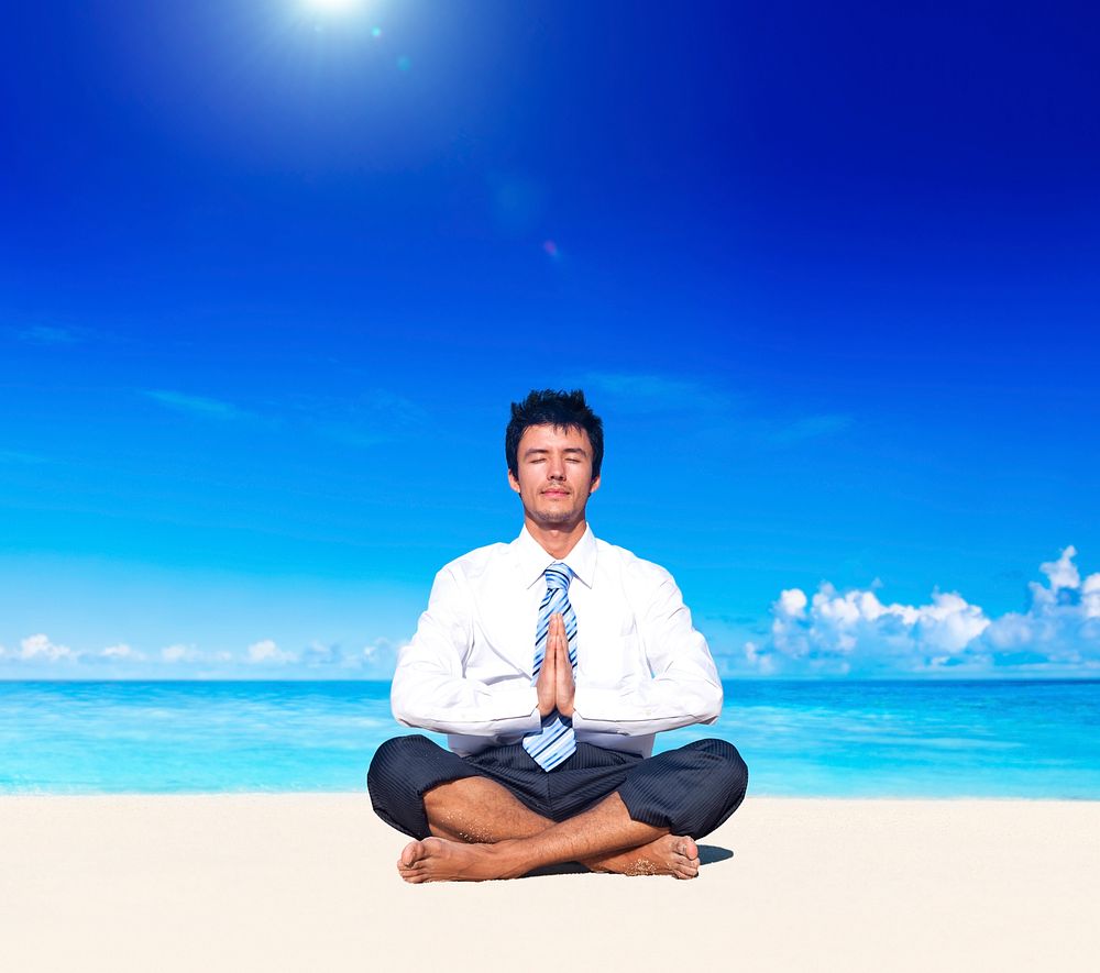 Businessman meditating on the beach.
