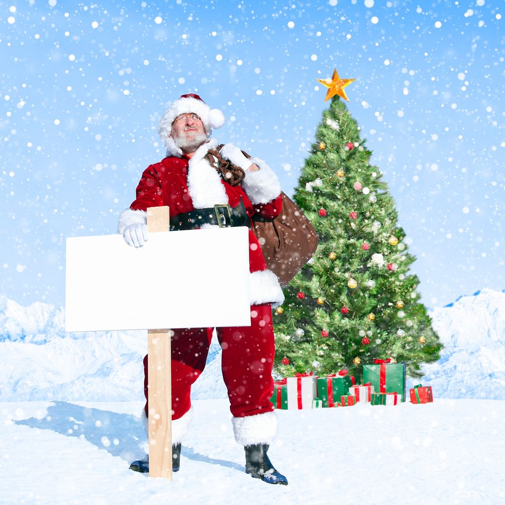 Santa claus holding sack and blank placard next to a christmas tree.