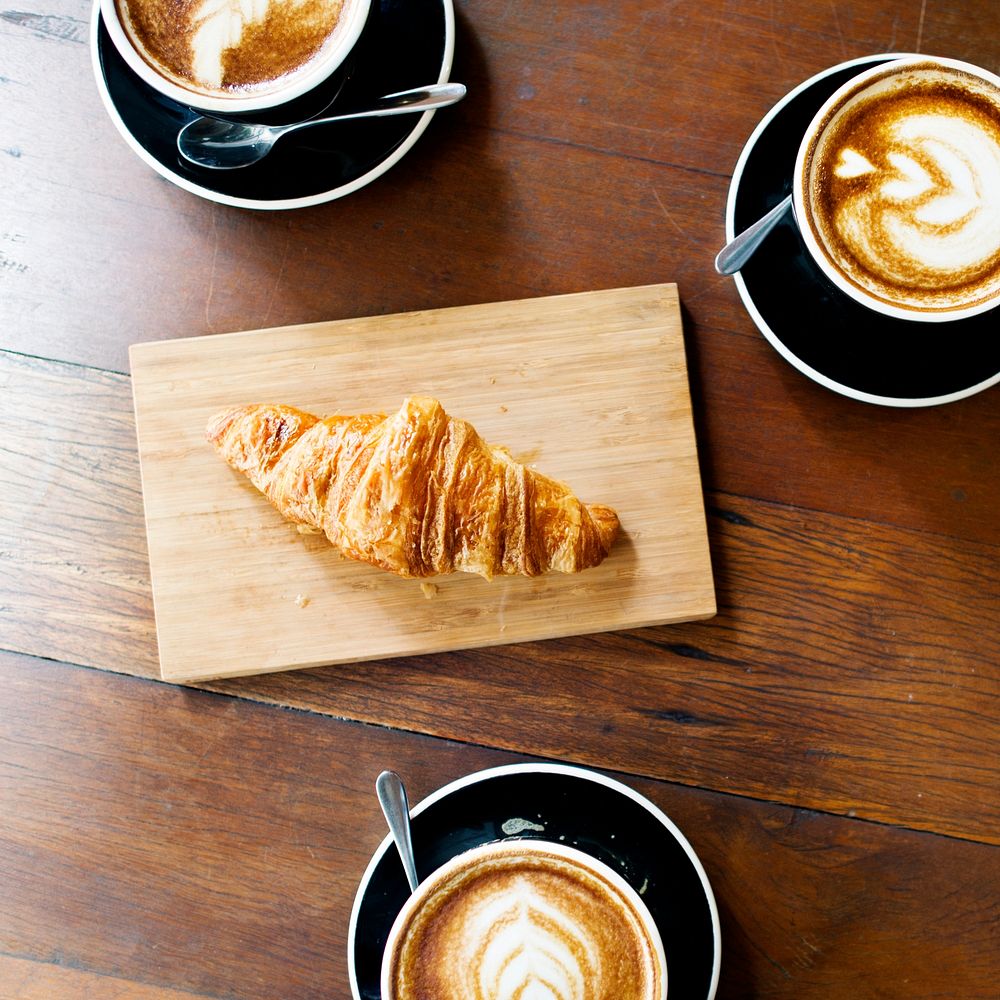 Aerial view of coffee cups and croissant on wooden table