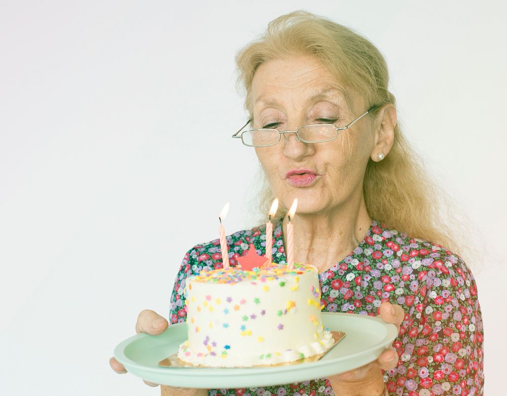 Senior Woman Hold Blowing Birthday Cake Studio Portrait