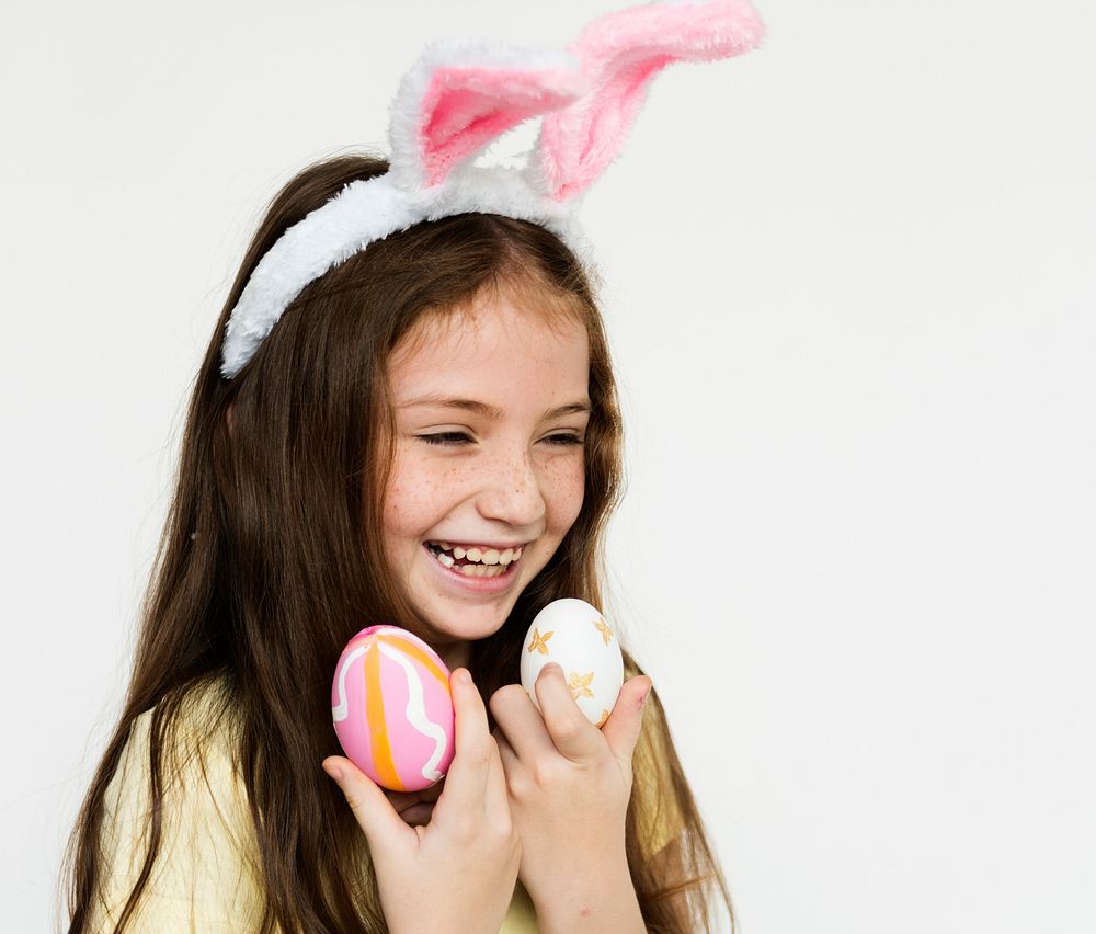 Caucasian girl wearing bunny headband and holding easter eggs with laughing