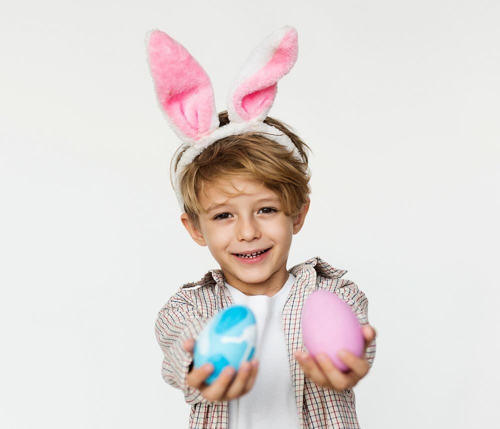 A boy is holing easter eggs and put pink bunny ear on.