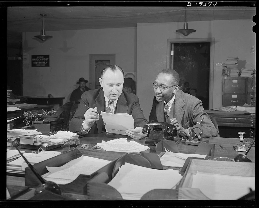 Office of War Information news bureau. Ted Poston, shown here with Elmer Roessner, chief of the general news desk, sees that…