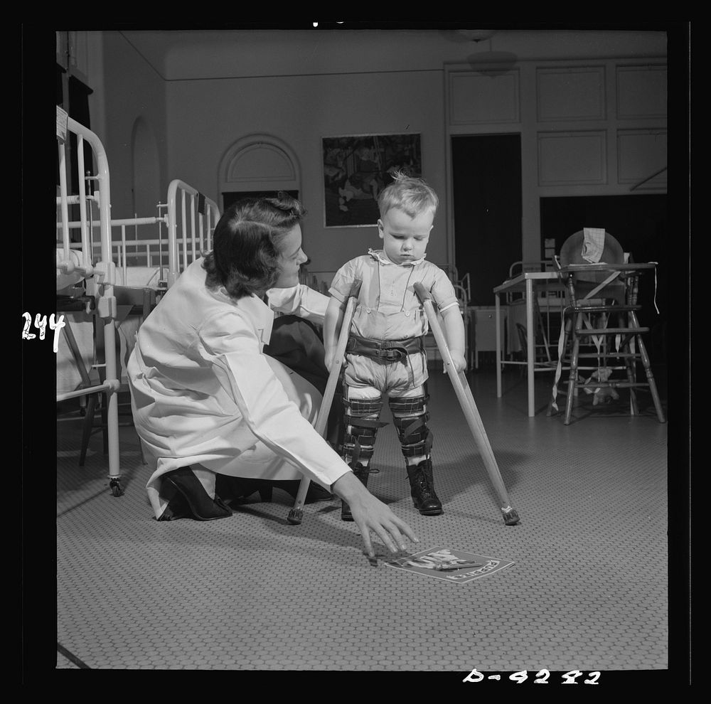 Nurse training. Using the picture book as bait, the physical therapist encourages a young victim of infantile paralysis to…