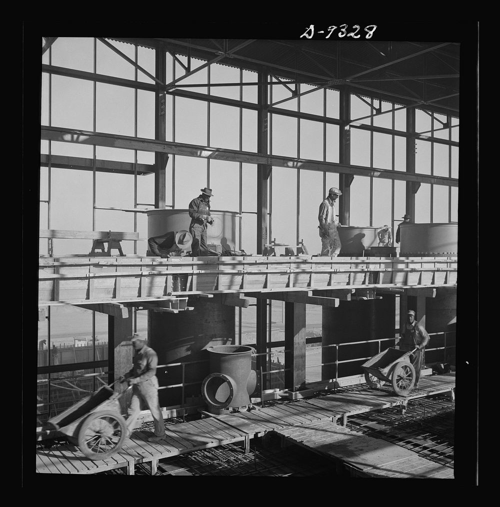 Production. Magnesium. High above the desert workmen speed up the reinforced steel construction of one of the 300-foot-long…