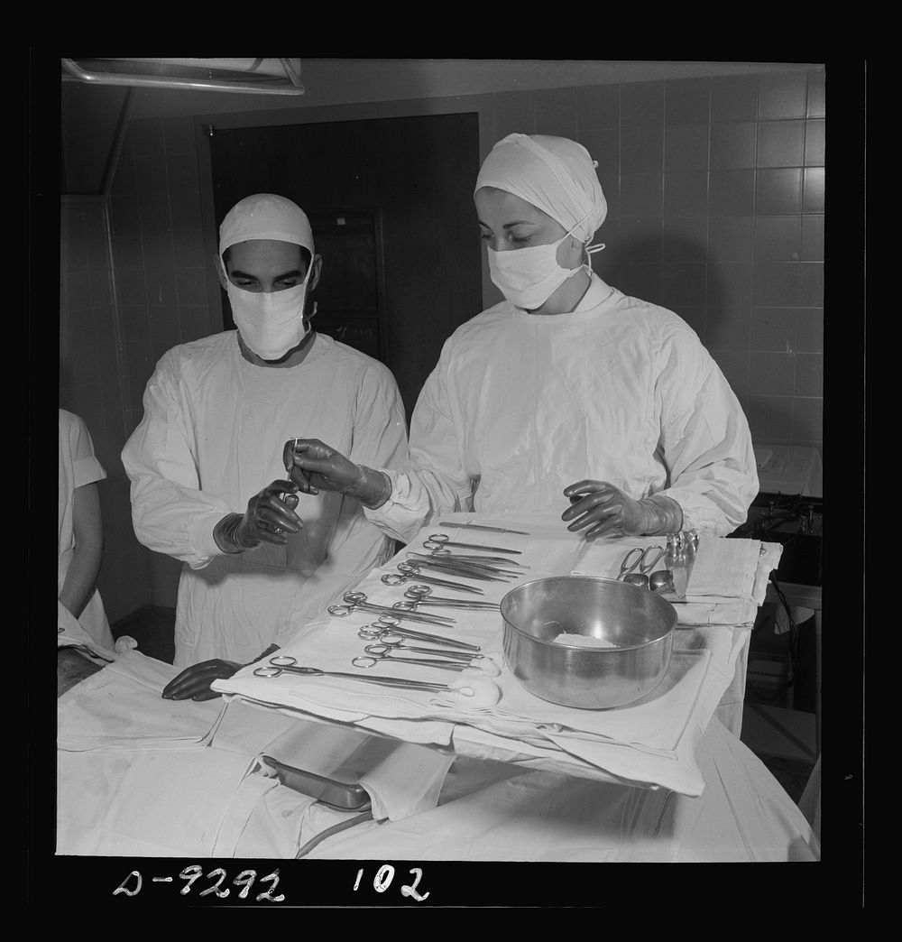 Nurse training. Assisting at an operation, a nurse hands a threaded needle to the surgeon who is about to perform an…