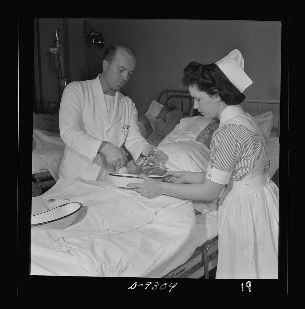 Nurse training. A student nurse assists the doctor in changing the dressing following an abdominal operation. Sourced from…