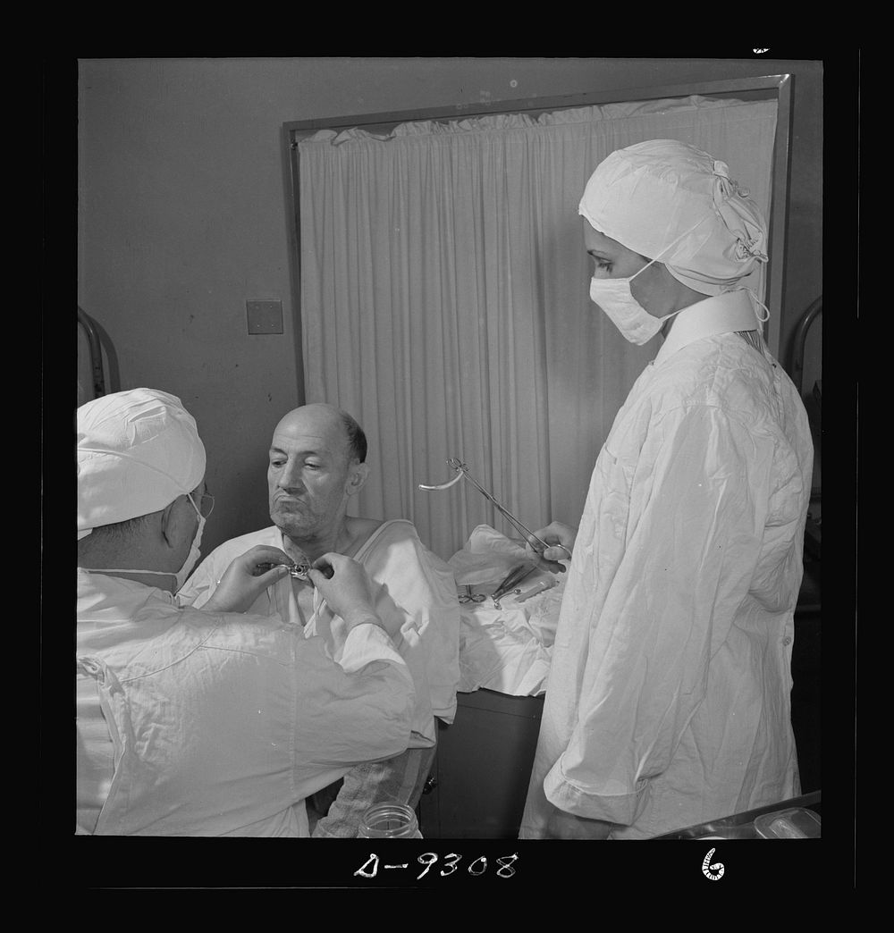 Nurse training. A student nurse stands by ready to assist the doctor as he changes a metal tube in a patient's throat…