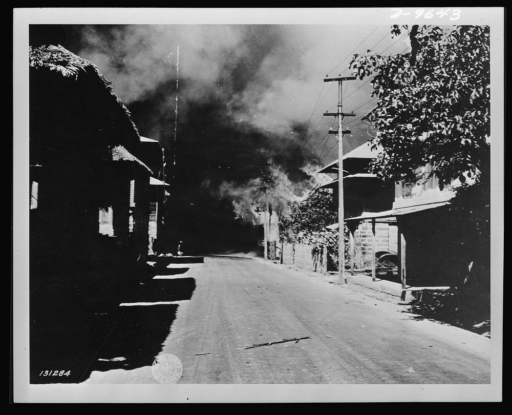 General view showing houses burning as the result of Japanese bombing raid in Bataan, the Philippine Islands. Sourced from…