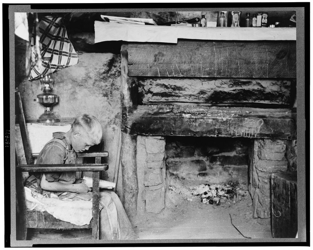 Mr. Leatherman's son reading in front of fireplace in dugout, Pie Town, New Mexico by Russell Lee