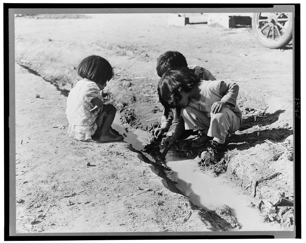 Mexican children playing in ditch which runs through company cotton camp near Corcoran, California. Sourced from the Library…